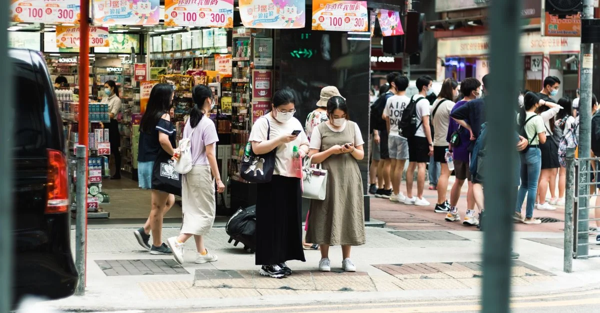Personnes portant des masques dans une rue animée près d'une entrée de magasin, utilisant des smartphones.