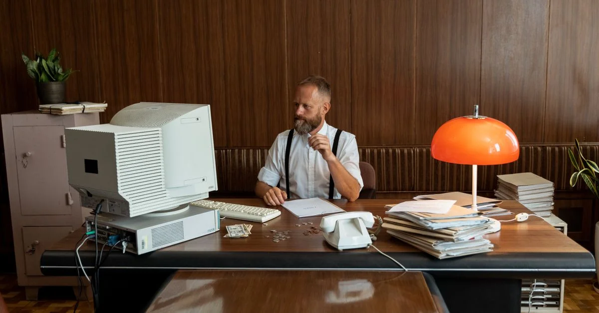 Homme dans un bureau vintage avec un ordinateur rétro et une décoration, incarnant l'ambiance des affaires des années 80.