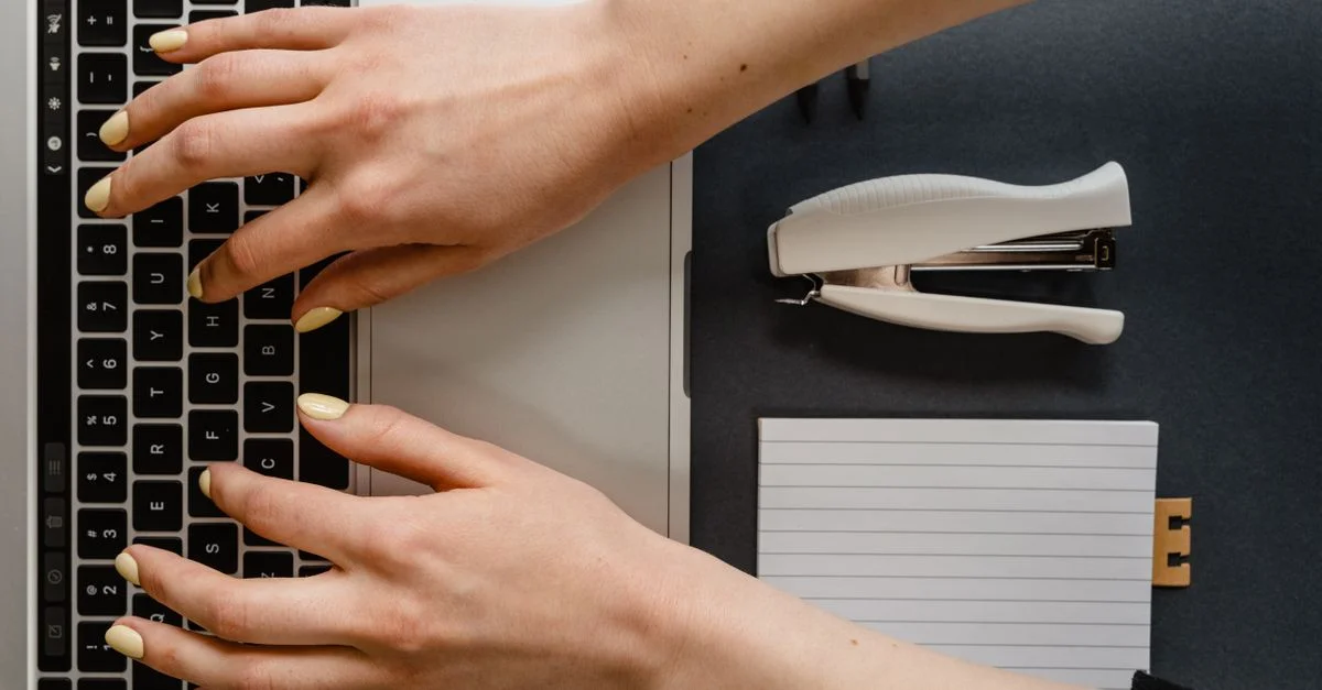 Vue de dessus des mains tapant sur le clavier avec des fournitures de bureau autour.