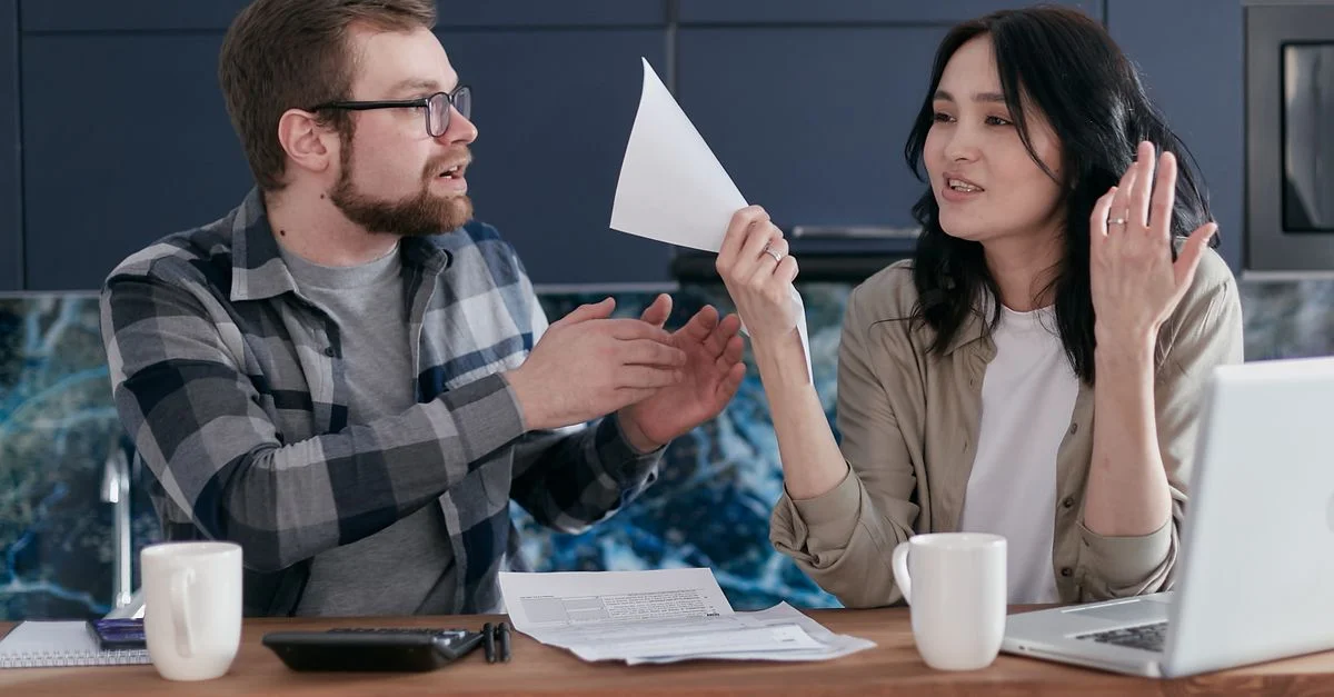 Un couple discutant de documents financiers à l'intérieur, avec un ordinateur portable et du café sur la table.