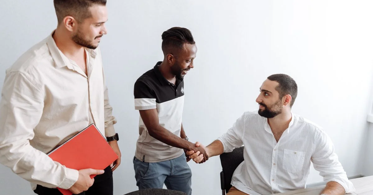 Trois hommes dans un bureau, se serrant la main, représentant le travail d'équipe et la diversité.