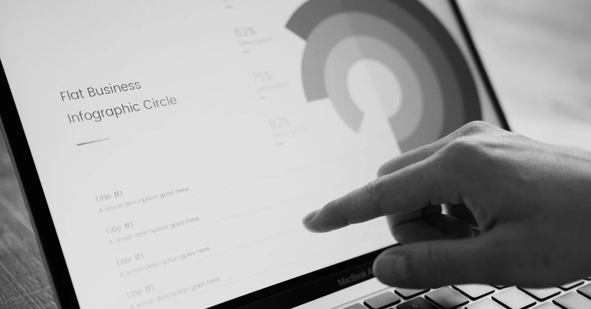 Doigt pointant sur un cercle d'infographie commerciale sur l'écran d'un ordinateur portable en noir et blanc.